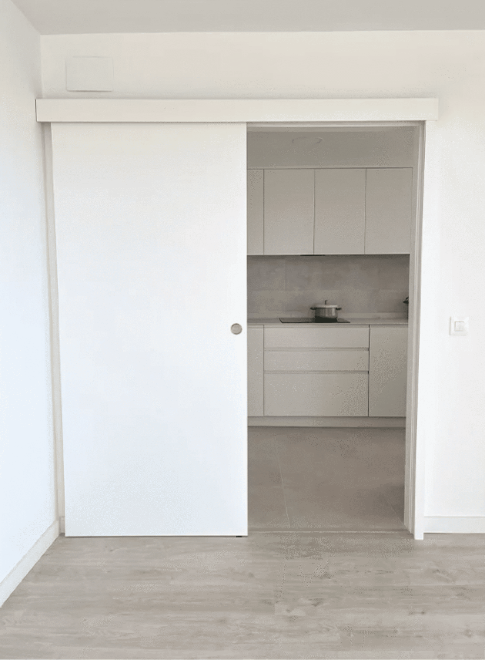 Puerta corredera de madera blanca para optimizar espacio entre cocina y salón.