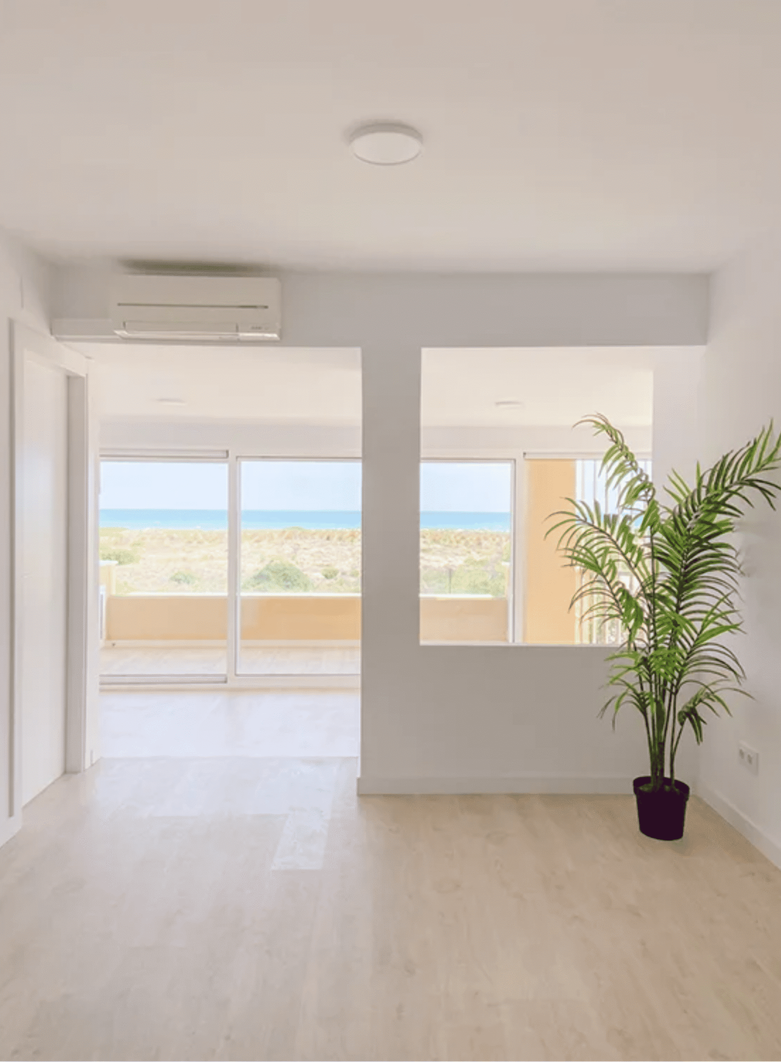 Salón diáfano con grandes ventanales, suelo de tarima clara y vistas al Mediterráneo.