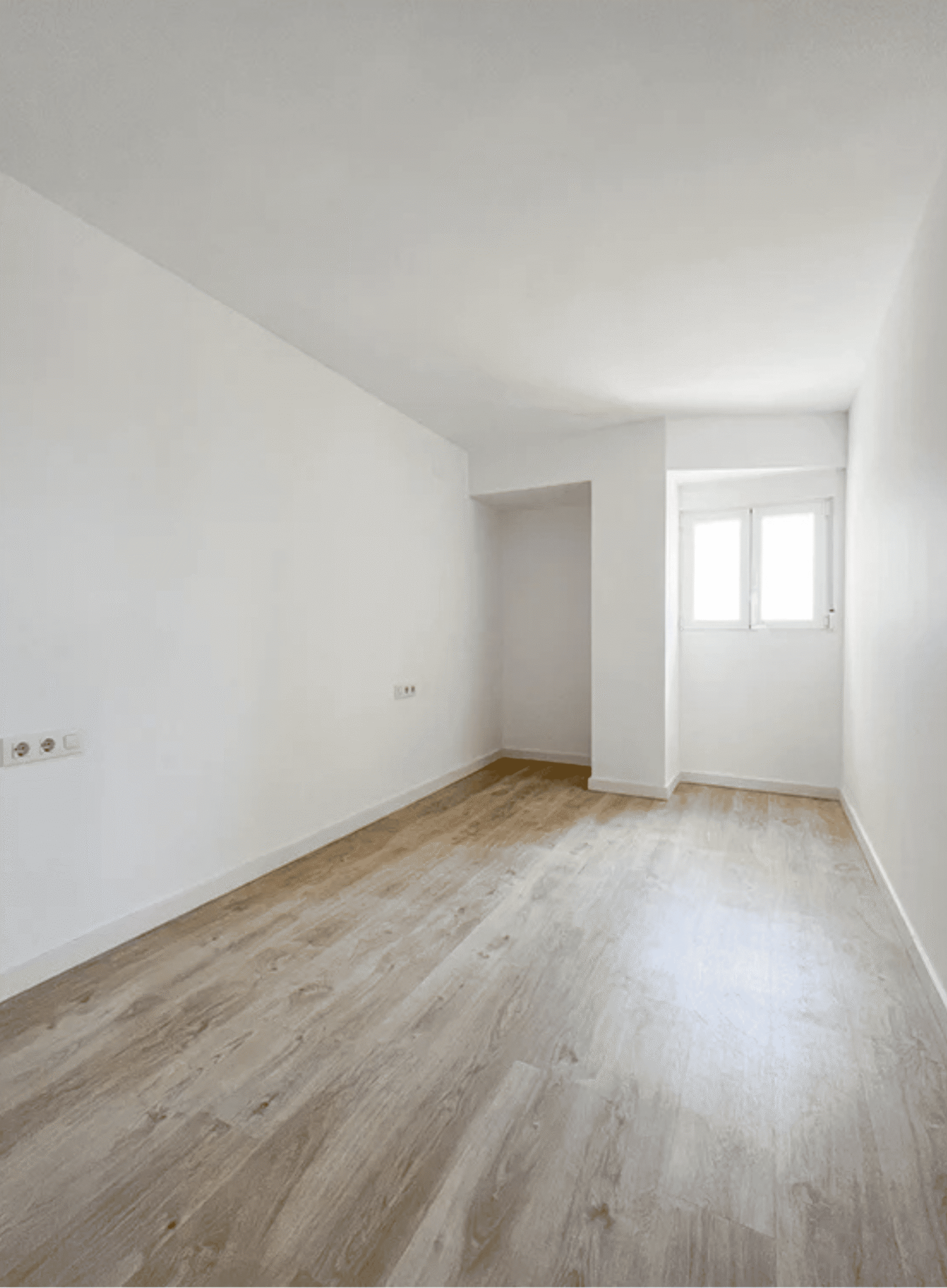 Habitación luminosa recién reformada con suelo de madera laminada y paredes blancas.