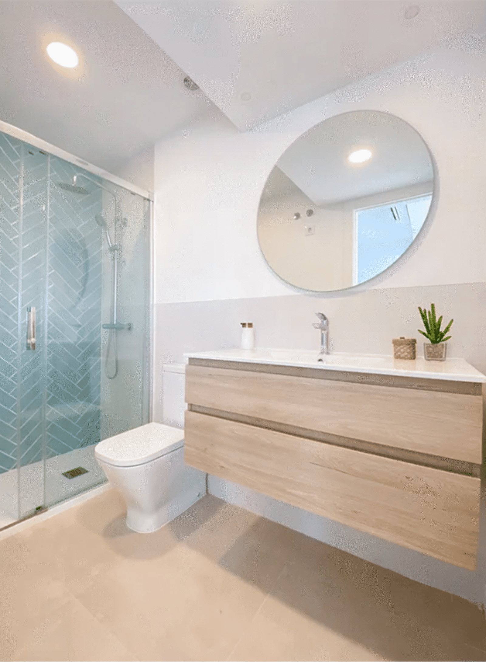 Baño moderno con mueble de madera, espejo circular y ducha con azulejos azul turquesa.