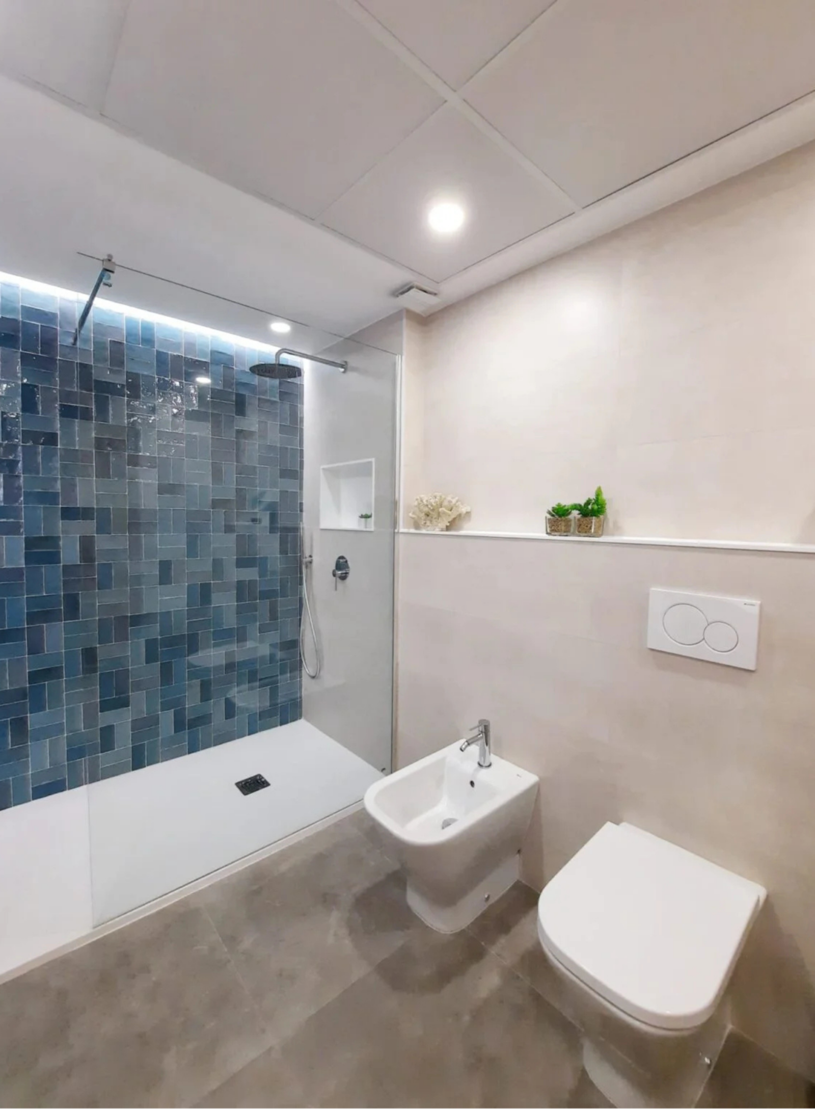 Zona de ducha con revestimiento de azulejos azules, rociador de techo y hornacina para geles.