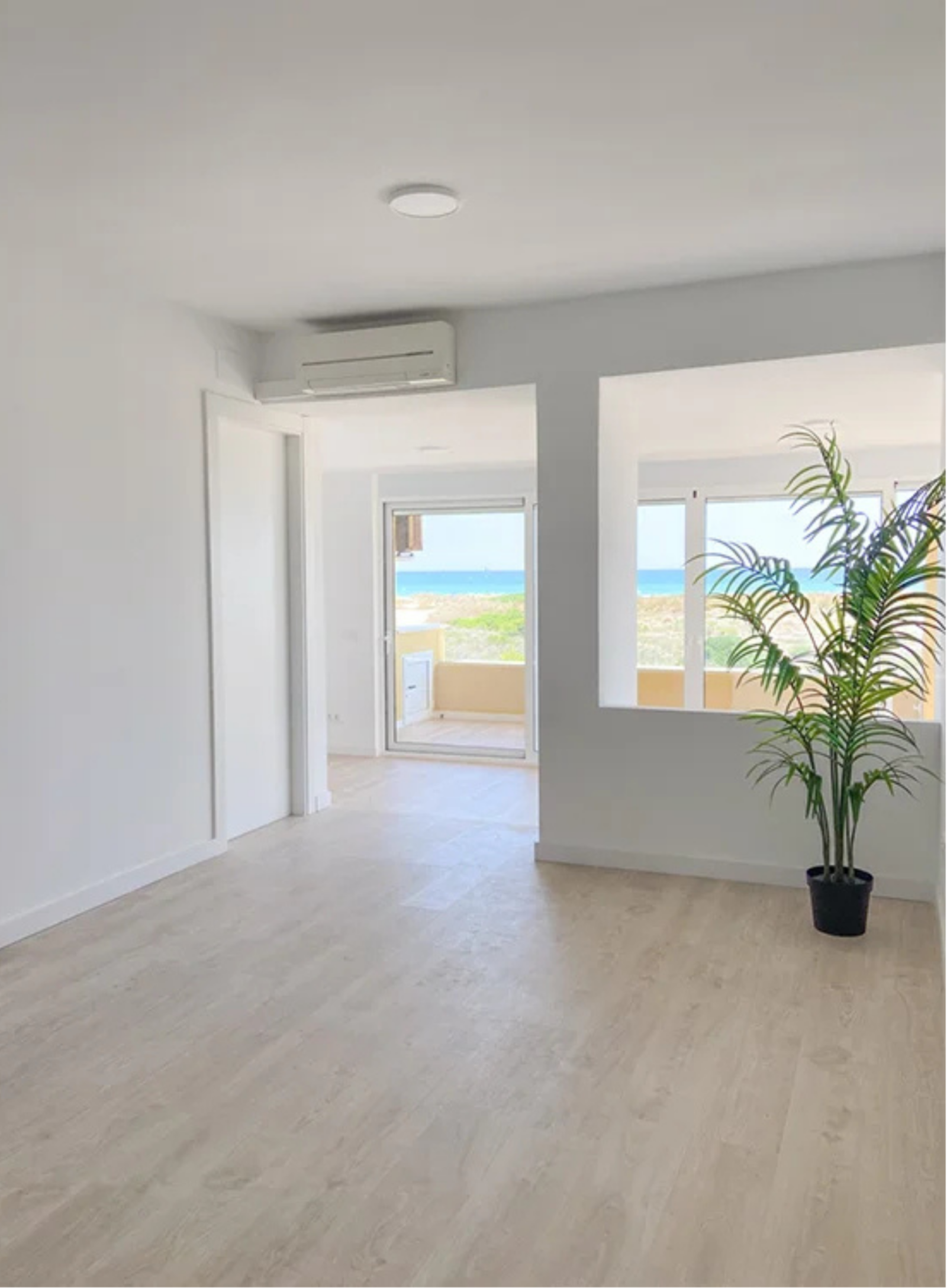 Salón diáfano con grandes ventanales, suelo de tarima clara y vistas al Mediterráneo.